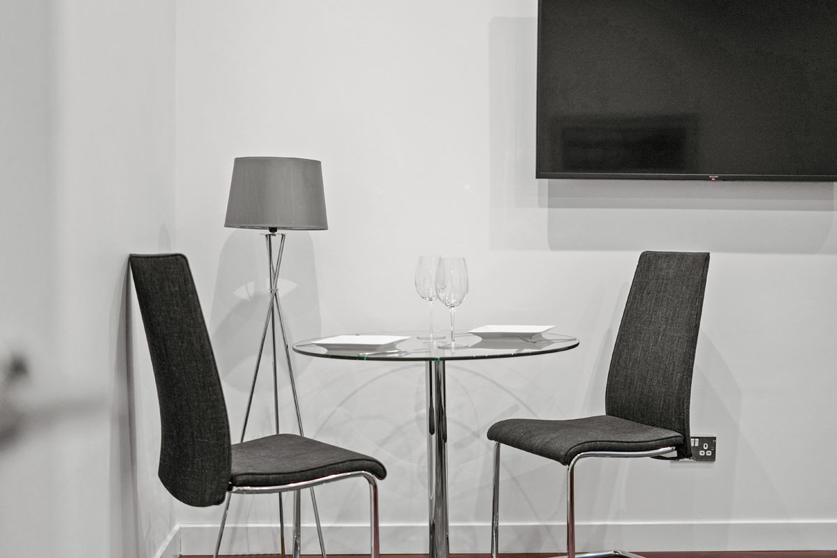 drinking glasses on top of a glass table with 2 chairs and a tv