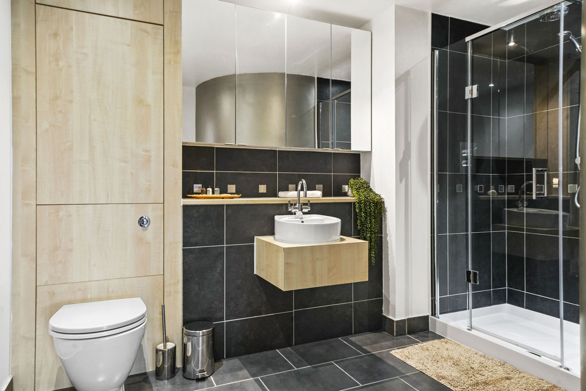 bathroom with natural color cabinets and dark gray tiles