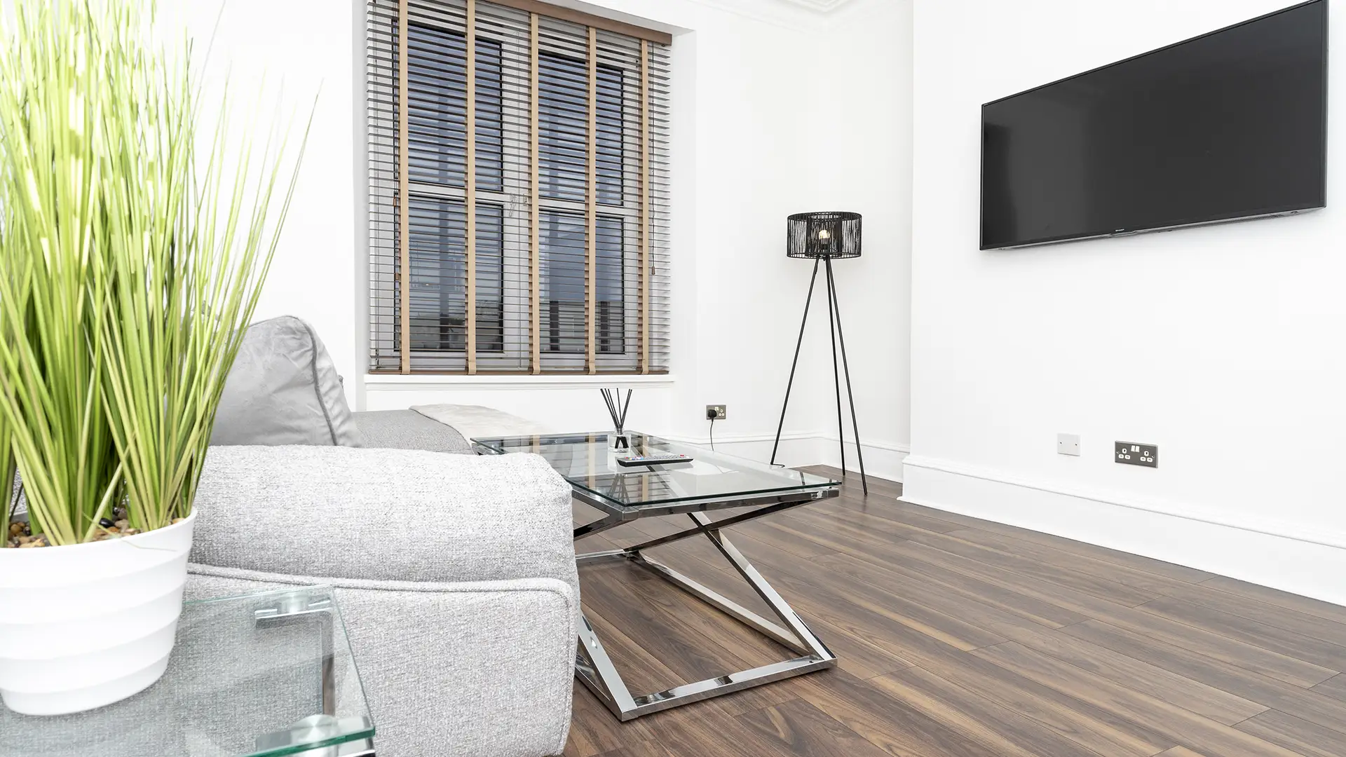 a large television mounted on a wall in front of a sofa set and glass center table